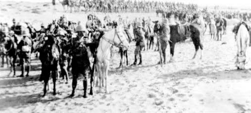 British mounted troops in the desert with camel-borne troops in the background.